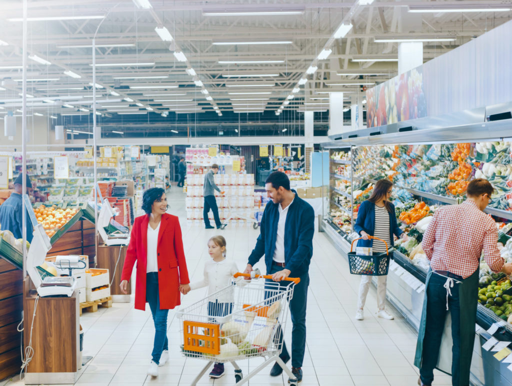 At the Supermarket: Happy Family of Three, Holding Hands, Walks Through Fresh Produce Section of the Store. Father, Mother and Daughter Having Fun Time Shopping. 