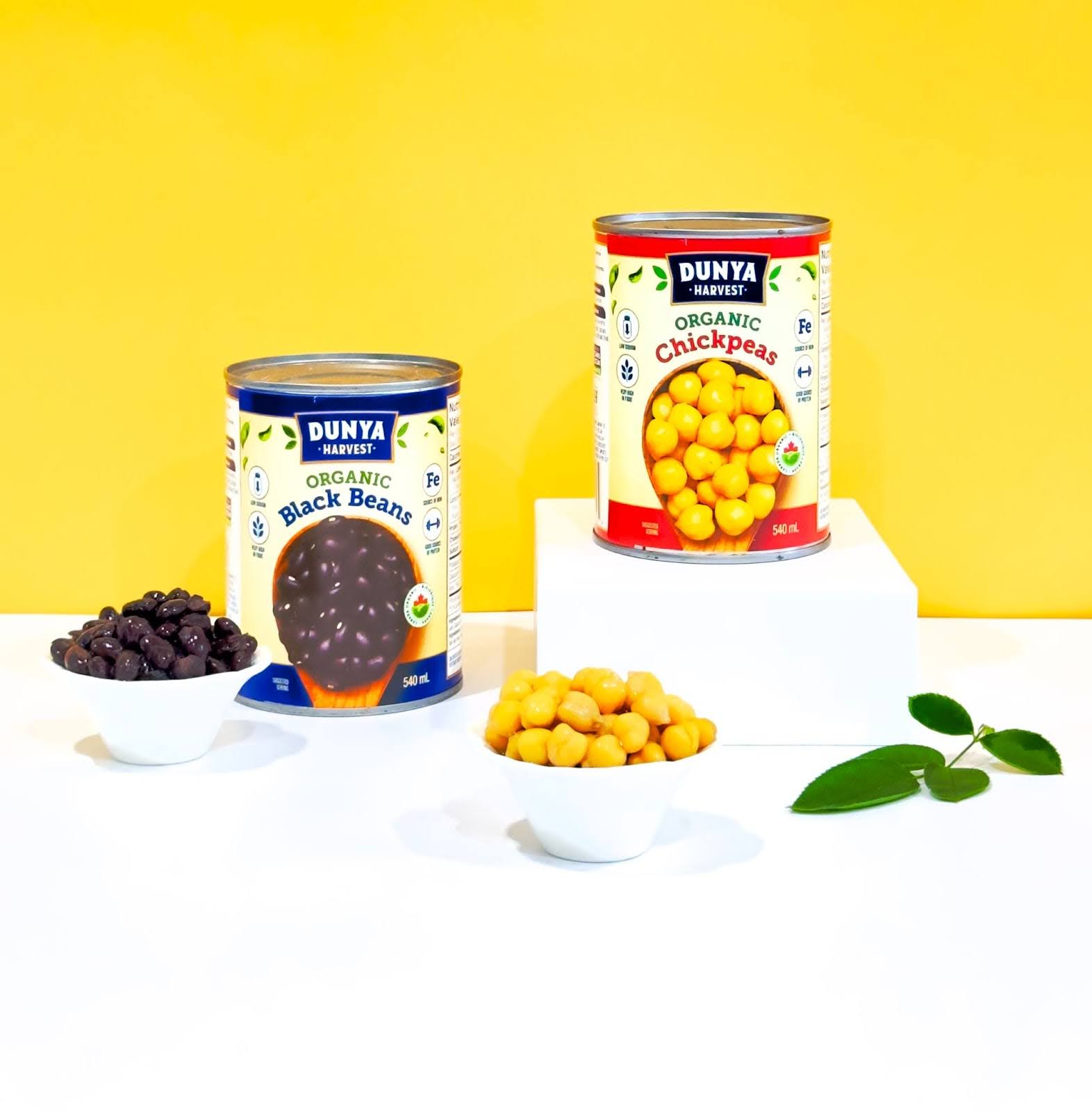 Cans of Dunya Harvest organic chickpeas and black beans against a yellow background.