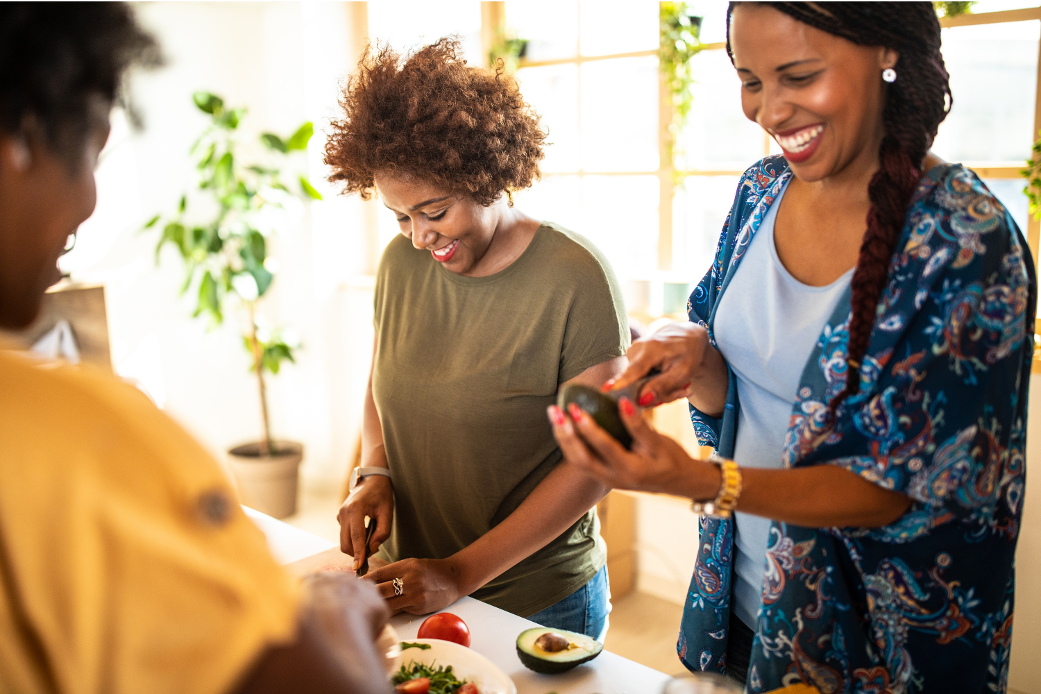 Three woman of color are standing and smiling cutting avocados