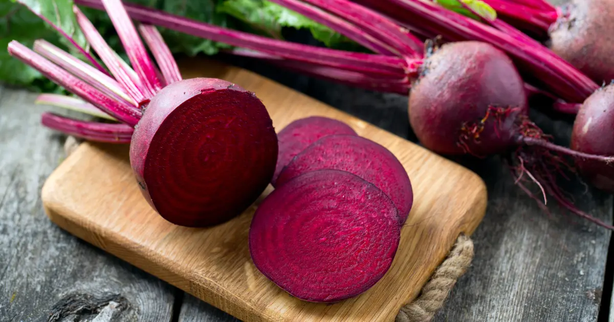 Freshly cut beets on a wooden cutting board beside a vibrant bunch of whole red beets