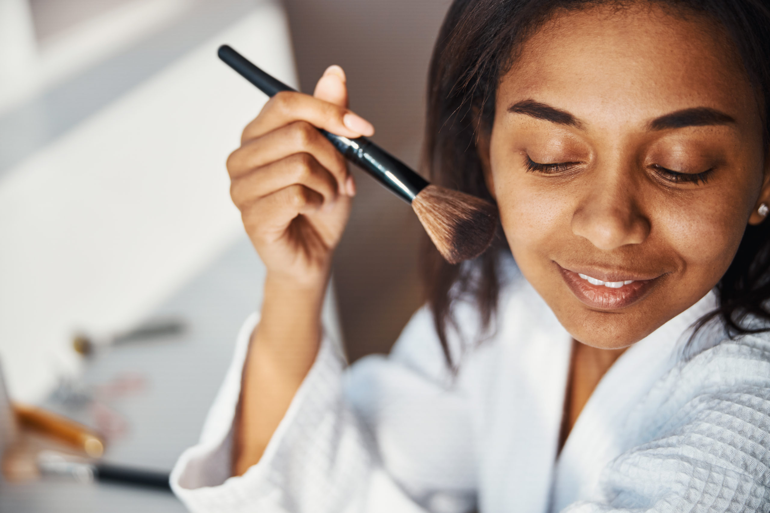 Close up of beautiful Afro American lady applying powder on face with cosmetic brush and smiling