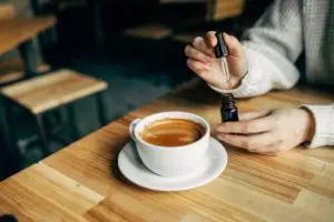 A woman holds a cup of coffee in one hand and a spoon in the other, ready to enjoy her drink.