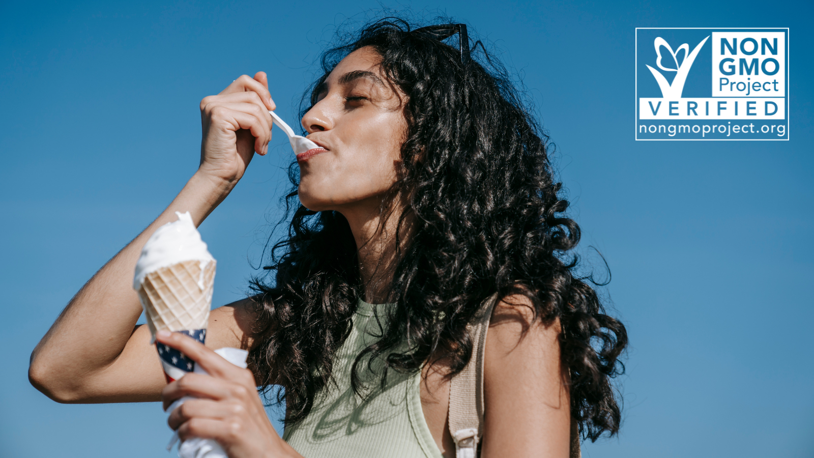 Curly hair woman of color eating ice cream from a spoon while holding ice cream cone