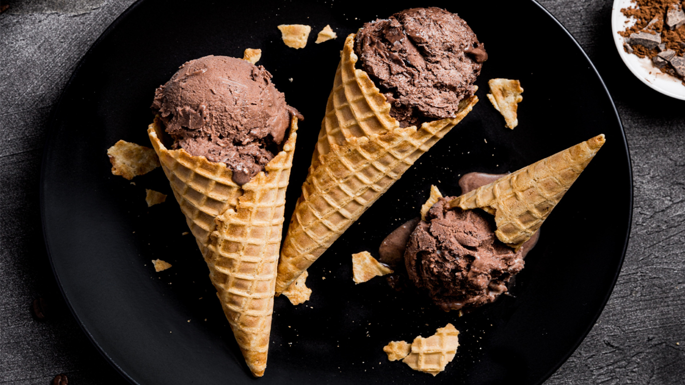 Three chocolate ice-cream cones laid flat on a black plate.