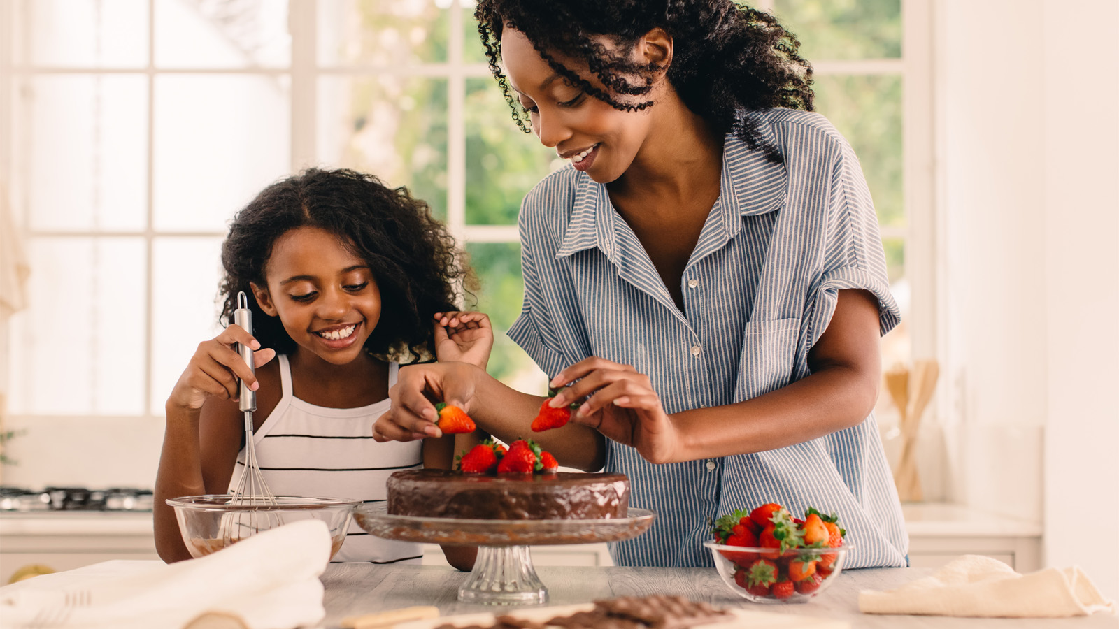 A woman of color decorating a chocolate cake with strawberries with her daughter