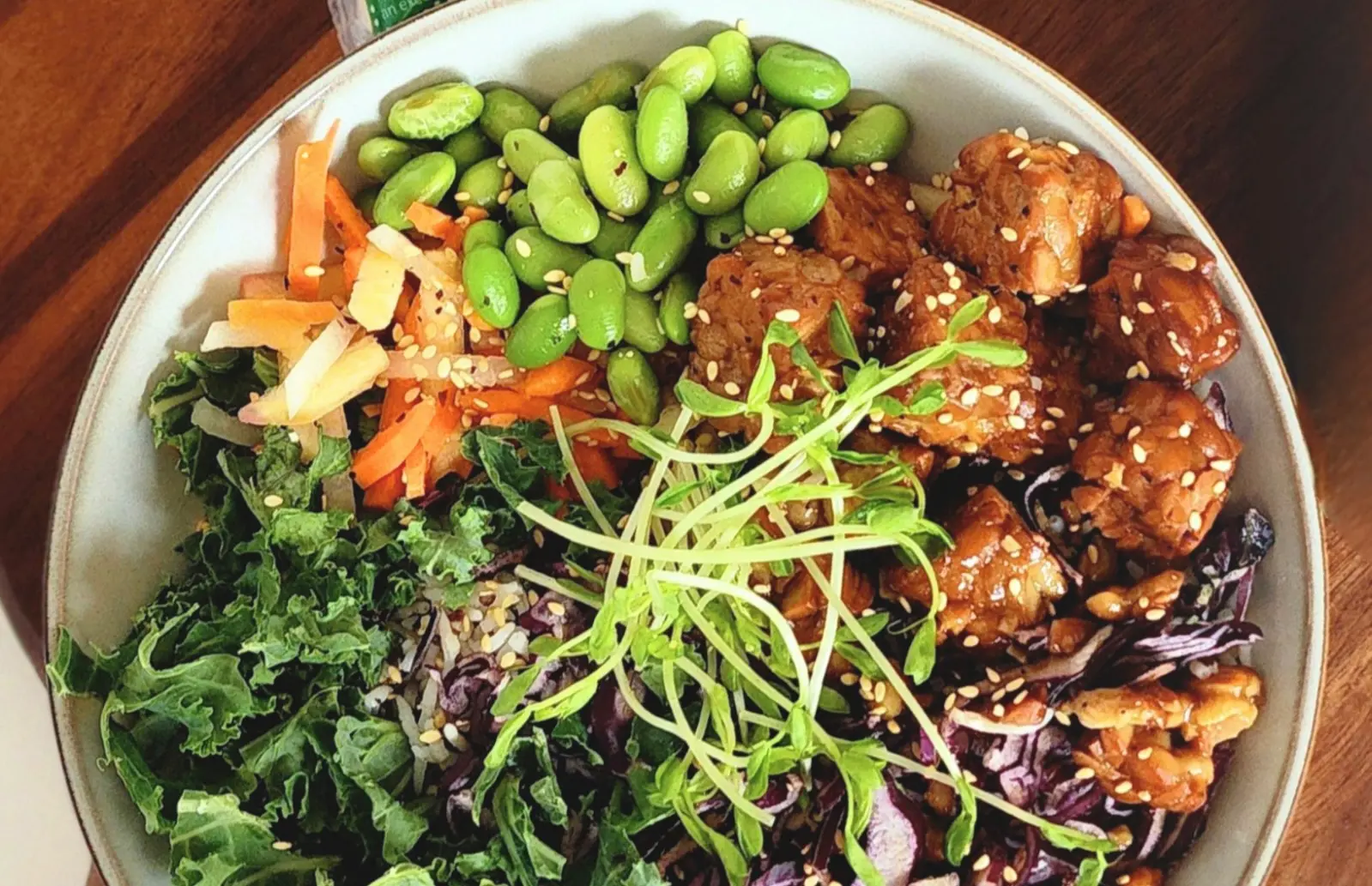 Bowl of tempeh, beans, mixed vegetables and sprouts, topped with sesame seeds.