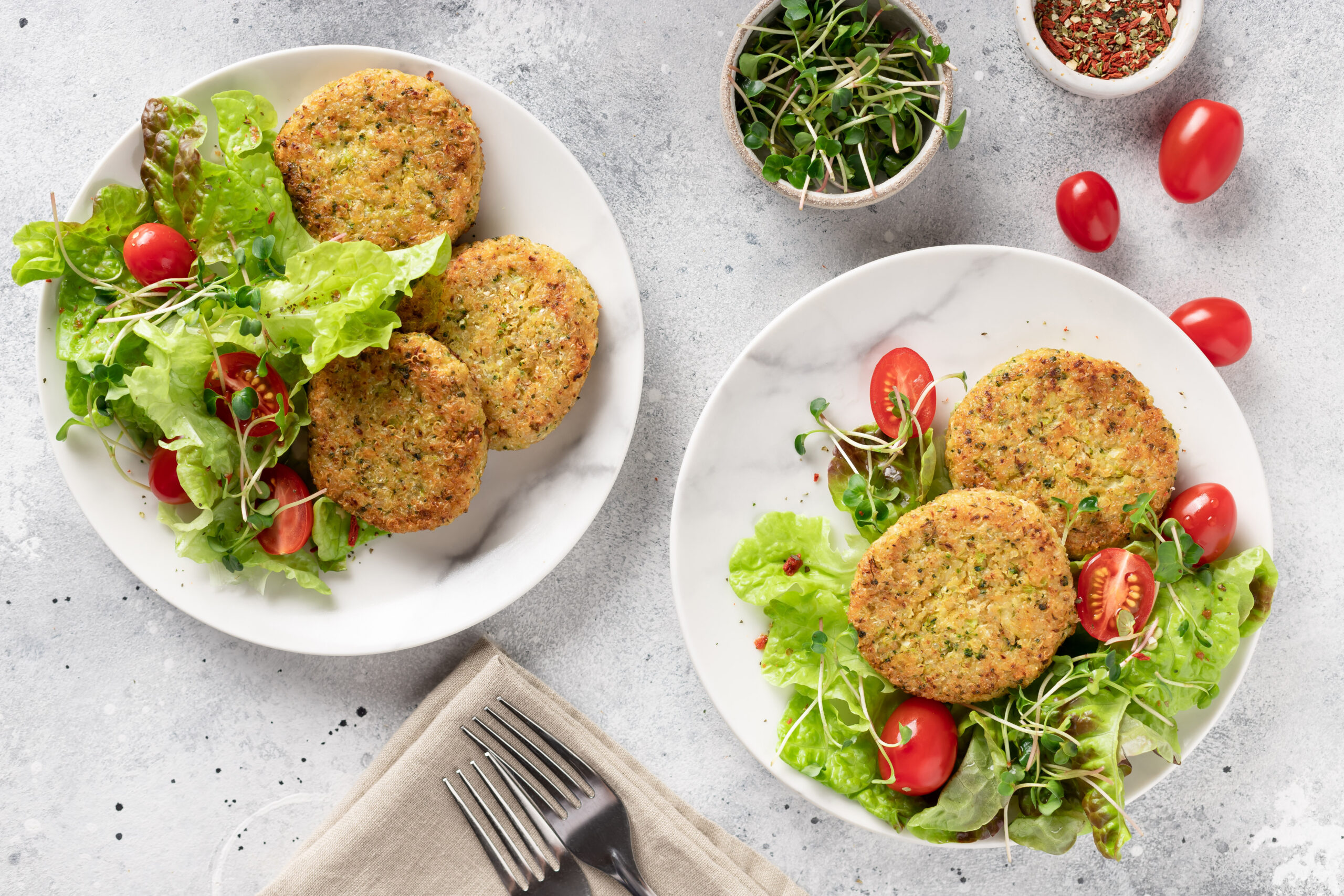 Vegan burgers with quinoa, broccoli in plates with salad. Vegan healthy lunch or dinner. Table setting.