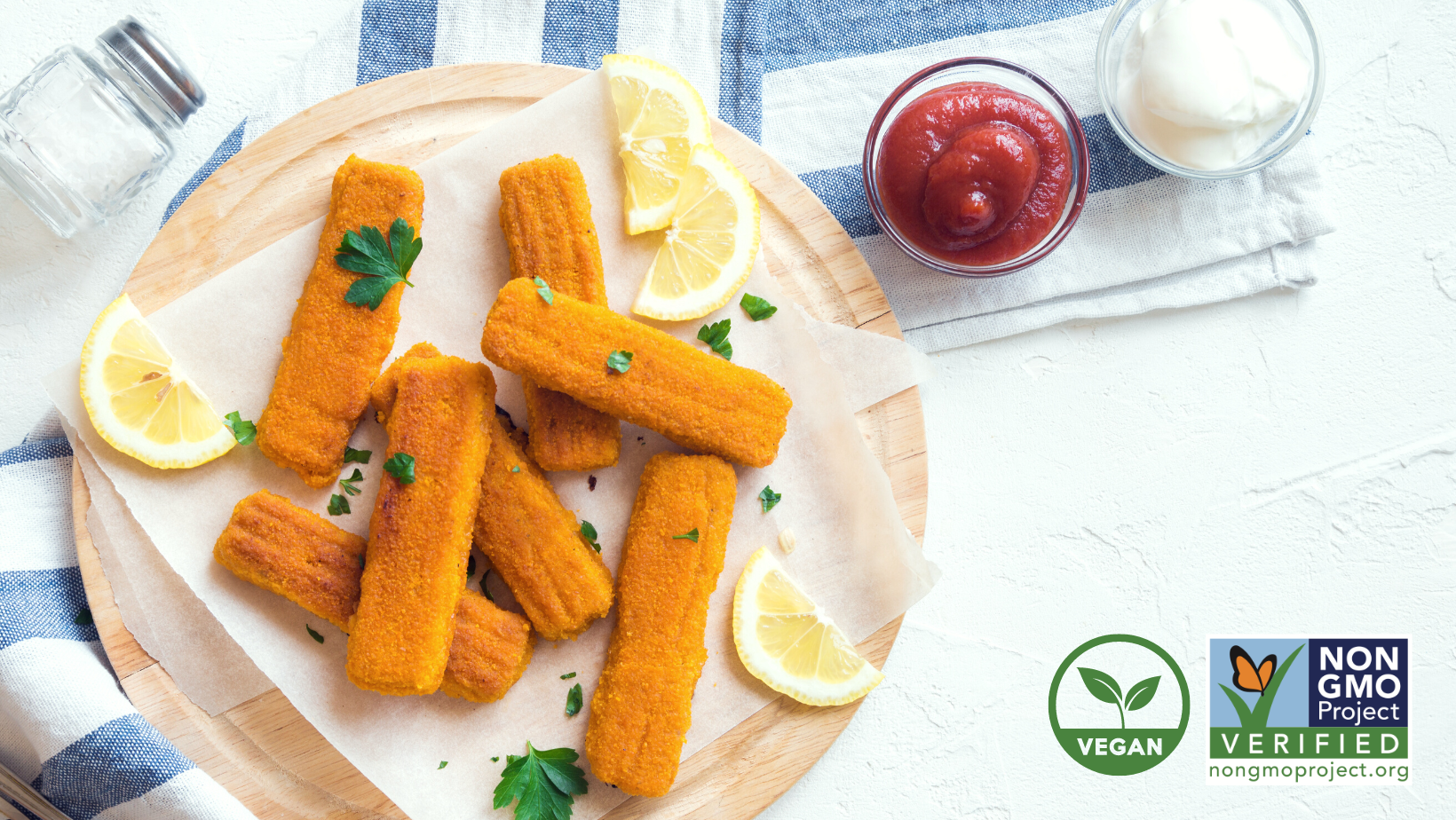 plant-based fishsticks on a wodden bamboo plate with herbs sprinkled on top and lemon wedges on the side