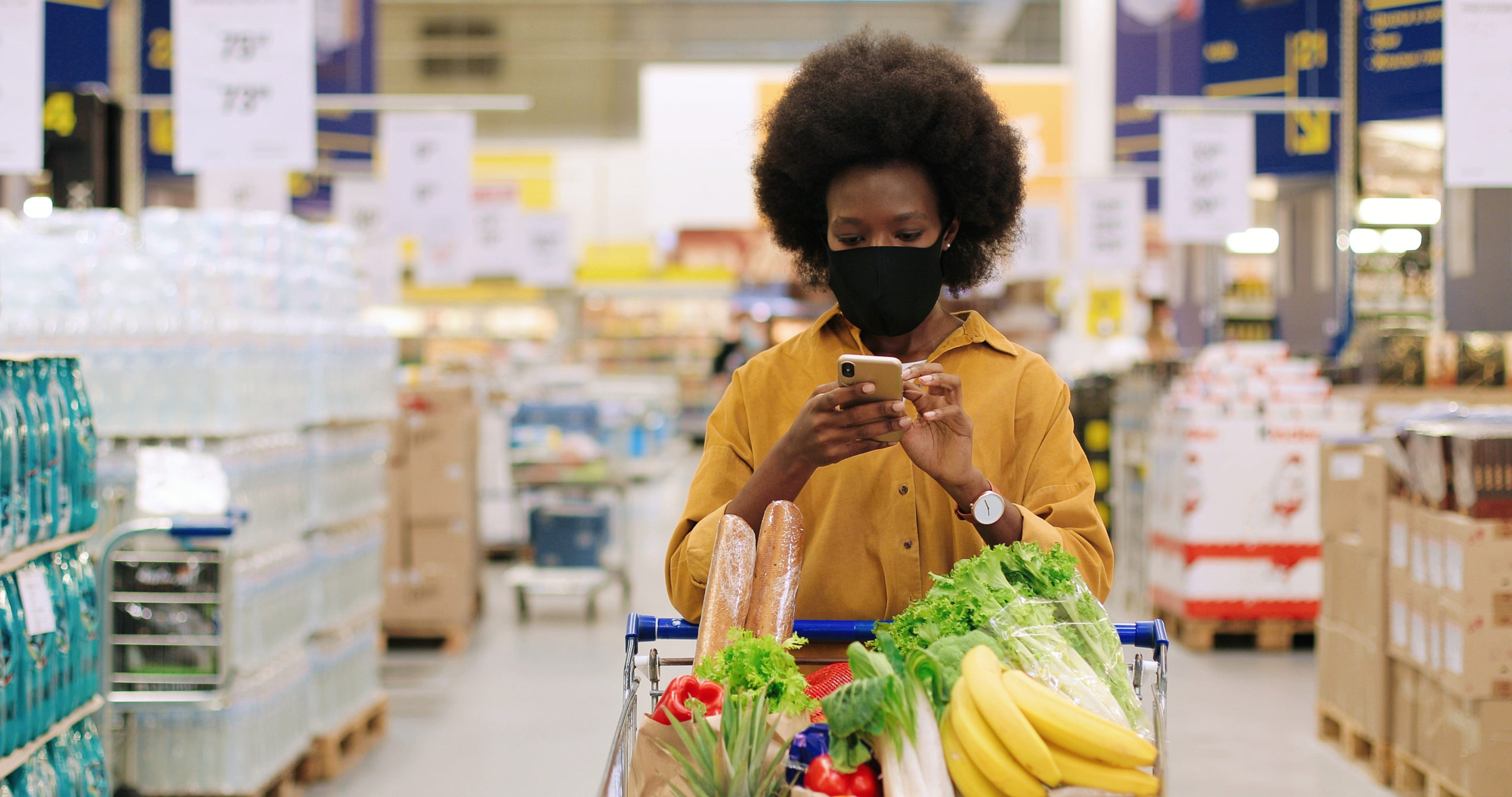 African American female in a grocery store on her cellphone standing behind her cart.