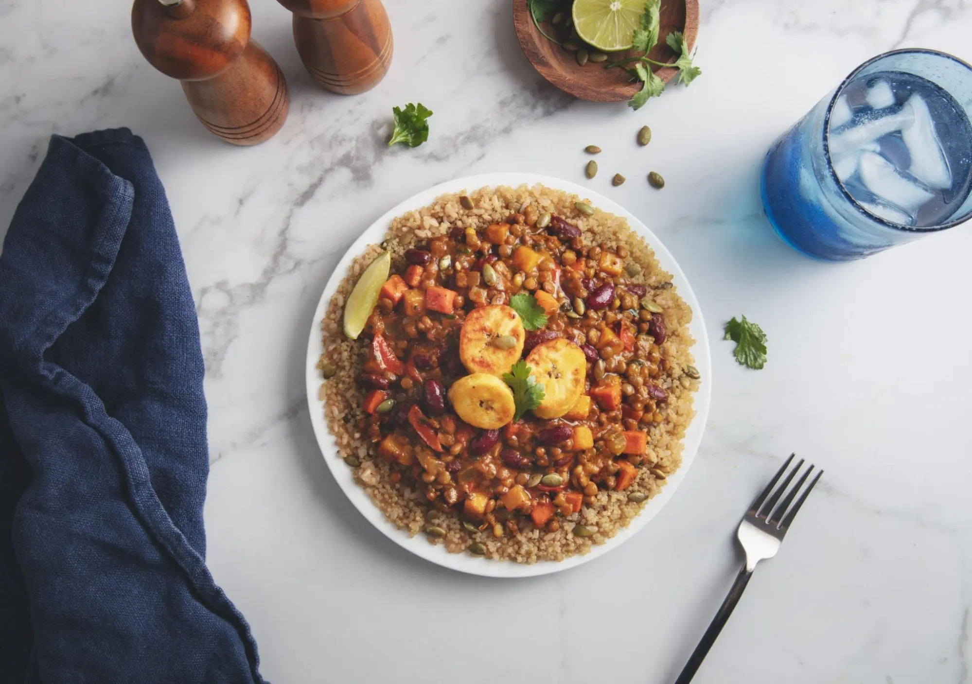 A vibrant and nutritious meal of quinoa and brown rice, accompanied by lentils, kidney beans, sweet plantains, butternut squash with Caribbean spices, served on a white plate.