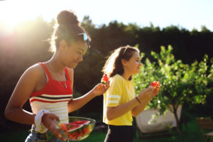 Side view of cheerful young teenager girls friends outdoors in garden, eating watermelon.